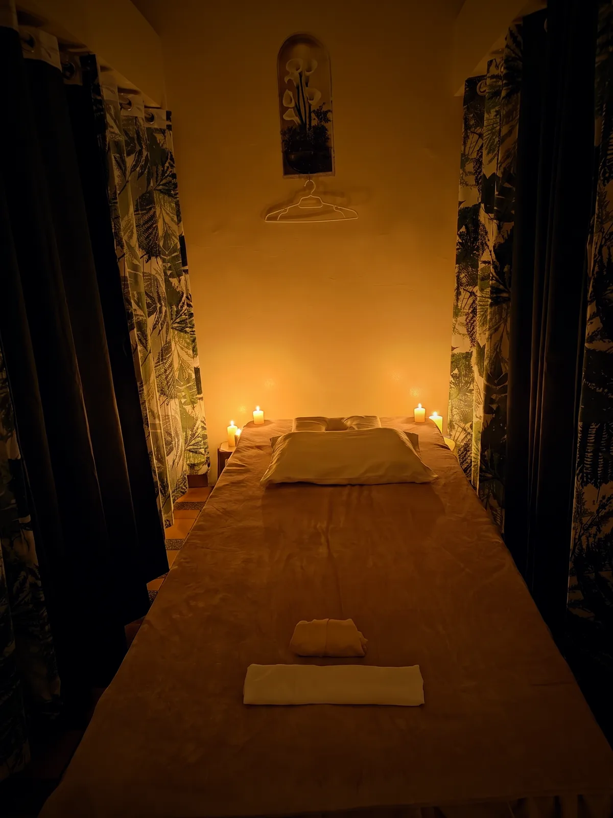 A private Dipolog Massage treatment room — a candle-lit massage table with fresh towels between leafy curtains