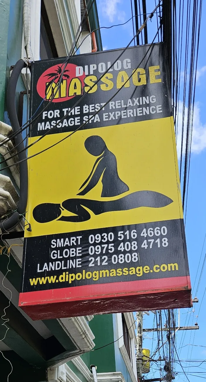 The old Dipolog Massage street signboard — bright yellow and red, with the tagline 'For the best relaxing massage spa experience'